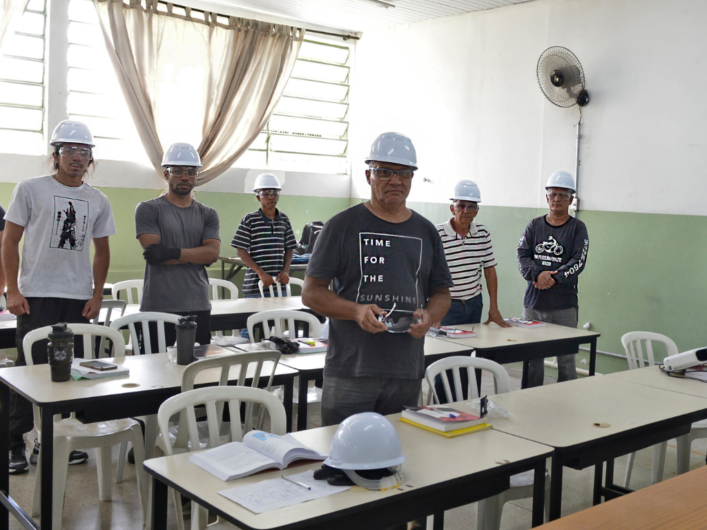 Na imagem, participantes de curso de eletricista realizado anteriormente, estão em pé, com EPIS - capacete e outros materiais necessários