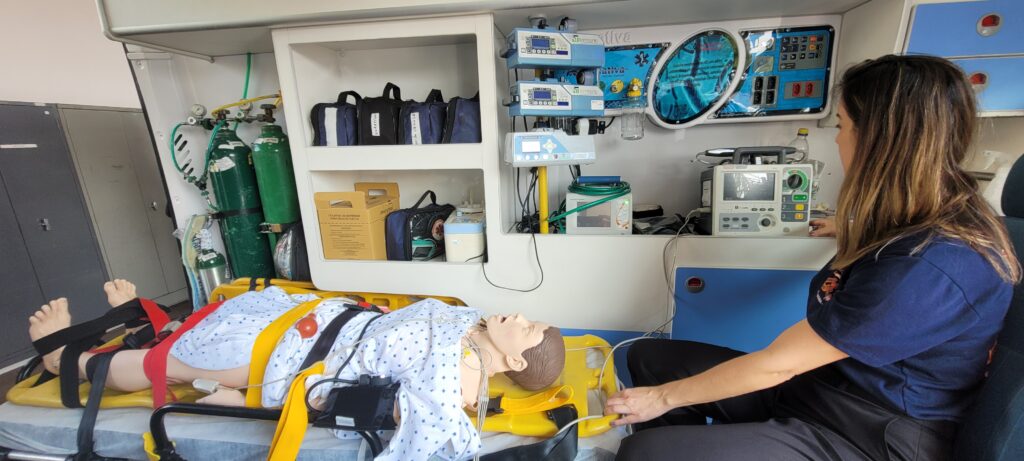 enfermeira Juliana está no interior de uma ambulância do Samu com manequim simulador fazendo demostração para o secretário de saúde