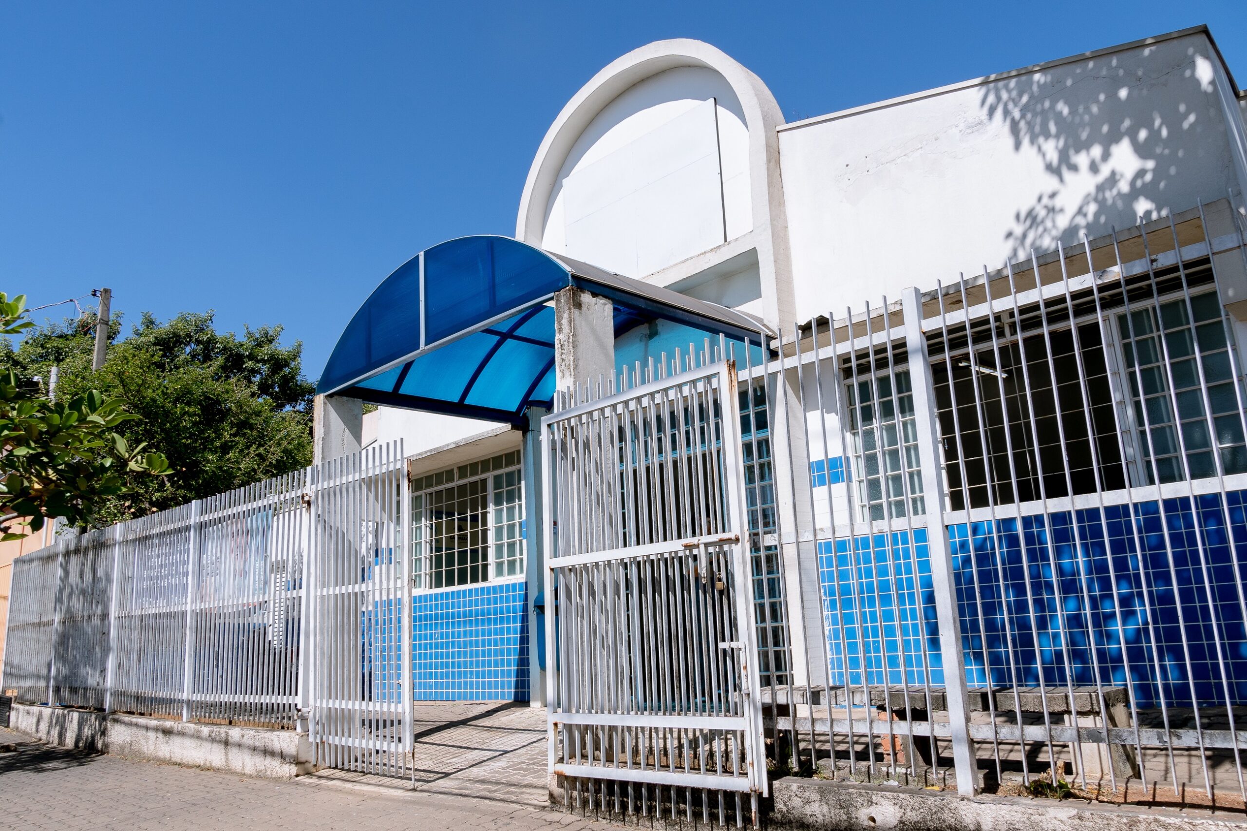 Imagem mostra a parte da frente da UBS Vila Cristina, com portão branco aberto e porta interna, de vidro, aberta para que as população entre na unidade