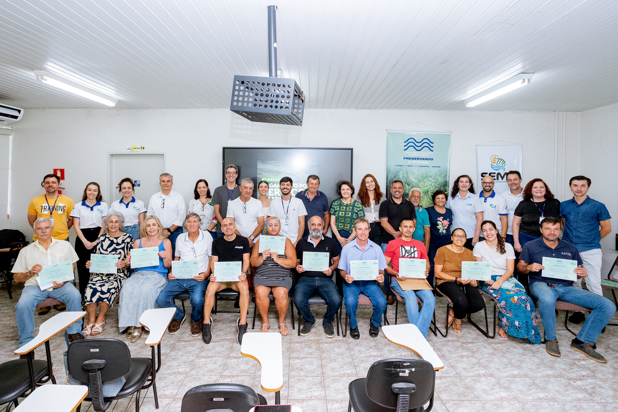 Agricultores sentados segurando o demonstrativo de pagamento do recurso e atrás de pé organizadores e parceiros.