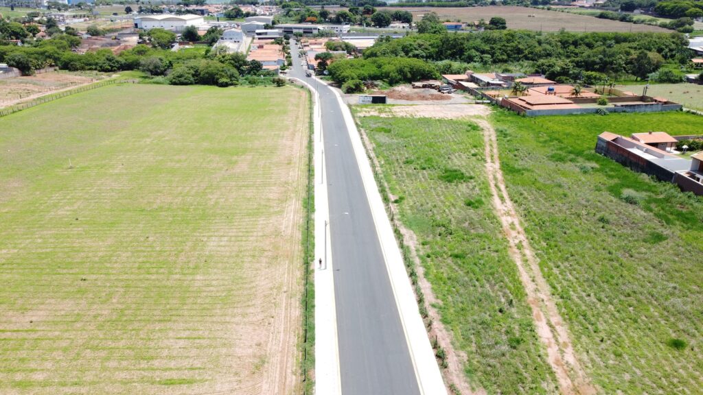Imagem aérea da rua Tim Lopes pavimentada; dos dois lados da via, há espaços com grama