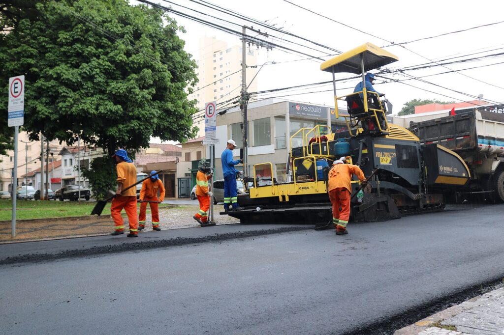 Trabalhadores com unifgorme laranja colocam pavimentação asfáltico na rua Alferes José Caetano.