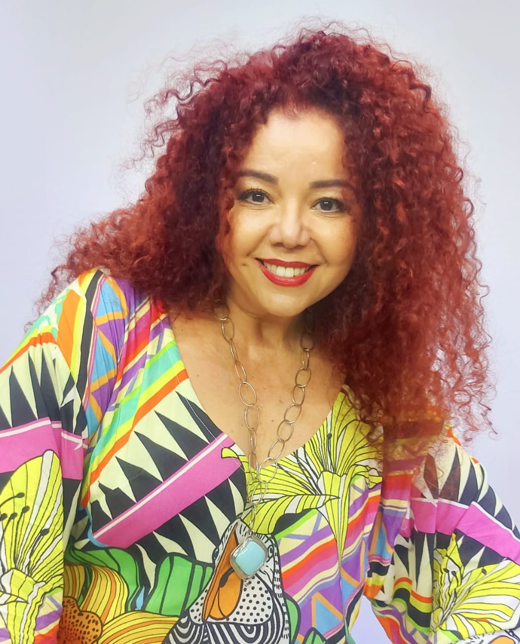 Cantora Santa Rodrigues, com cabelo cacheado vermelho e de vestido estampado colorido