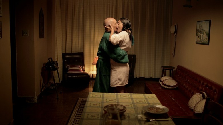 Um homem e uma mulher se beijam em uma sala na penumbra