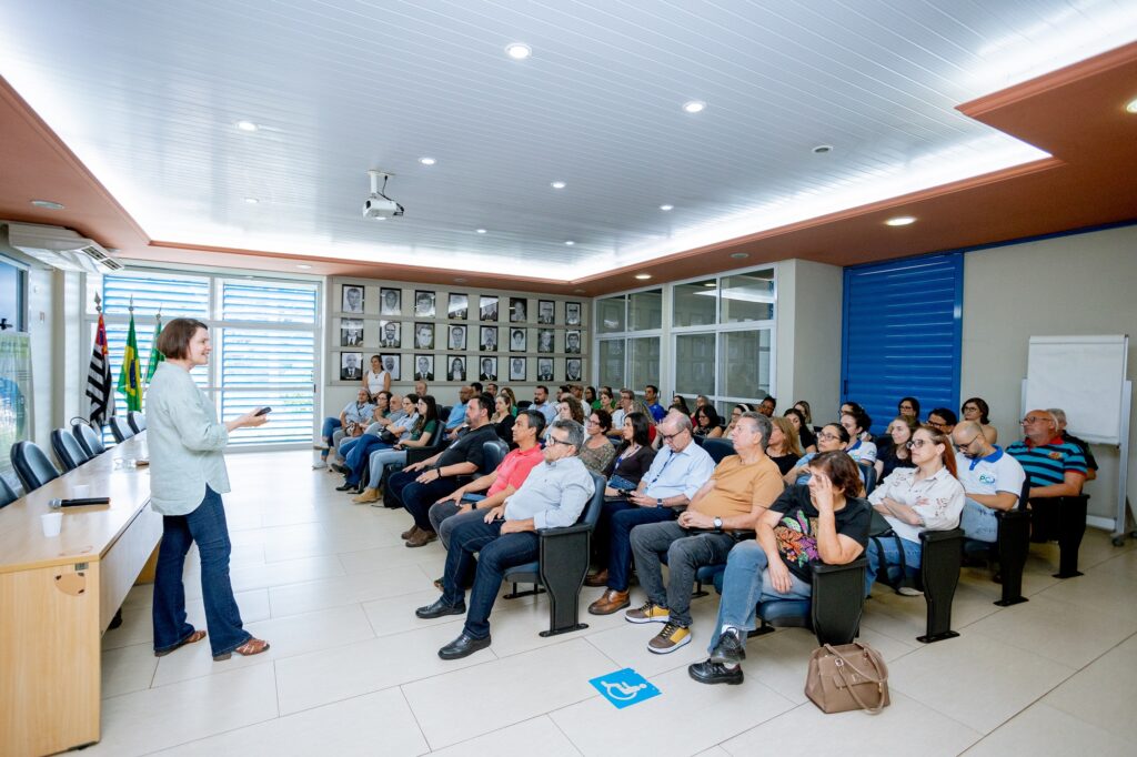 Platéia devidamente sentadas em poltronas escuras, ouve atentamente explicações da secretária municipal de Agricultura e Abastecimento (Sema), Nancy Thame, que está de camisa azulk clara e calça jeans escura.