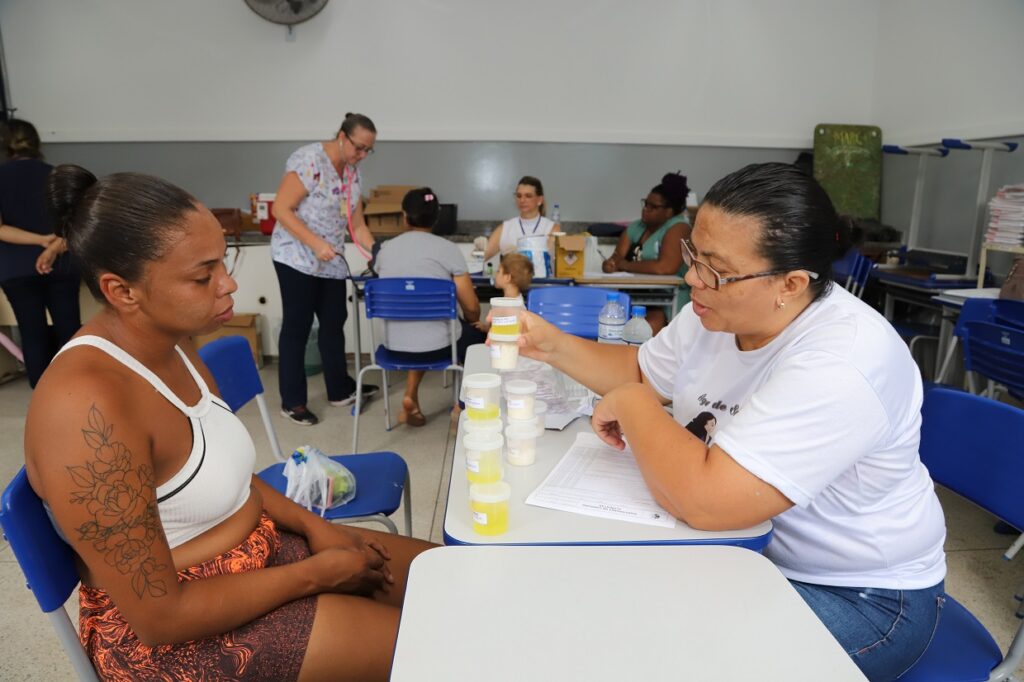 Mulher observa outra mulher mostrando potes que demonstram quantidade de açúcar em alimentos