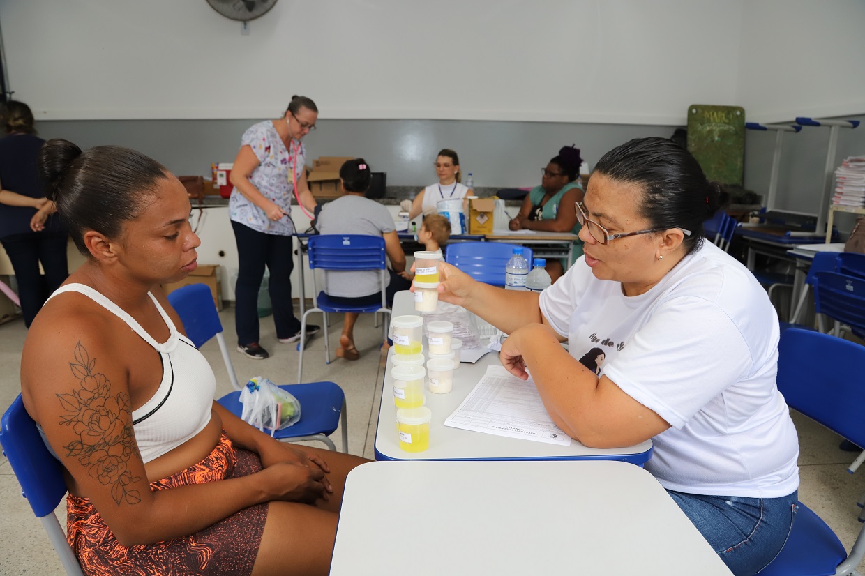 Mulher observa outra mulher mostrando potes que demonstram quantidade de açúcar em alimentos