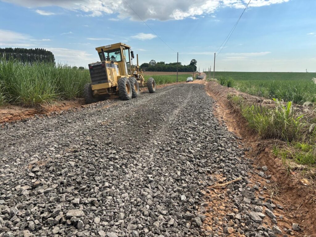 Trator estacionado em acostamento em estrada rural com lajão britado. Nos dois lados aparecem a vegetação no solo.