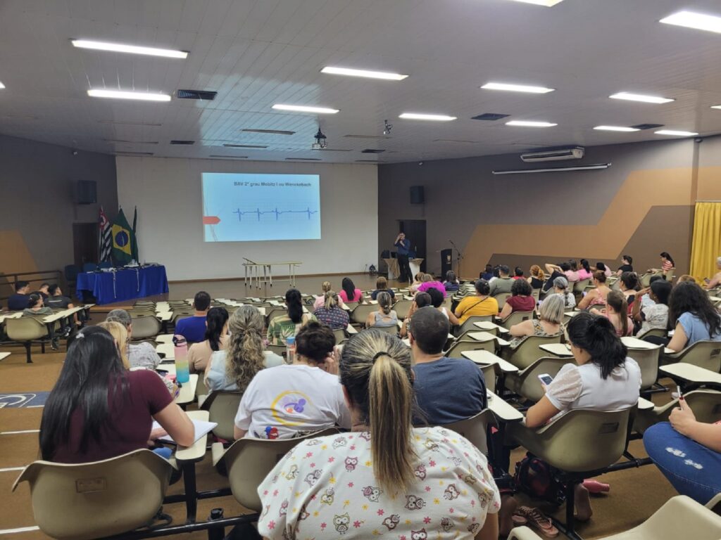 Médico olhando para a platéia formada por enfermeiras, que estão sentadas, explica procedimentos necessários , no cuidado compacientes.