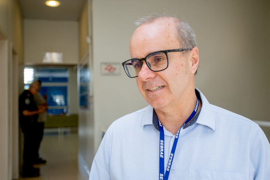 Senhor calvo de óculos com camisa azul clara, com crachá do Sebrae, entidade que representa.