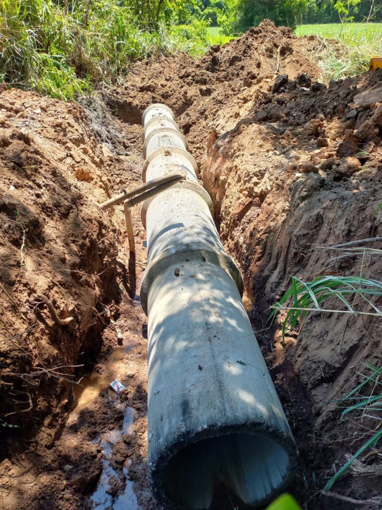 Tubo de concreto sendo aterrado em estrada rural.