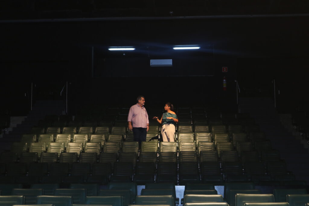 Um homem, o secretário Beltrame, e uma mulher, diretora Luana, em meio a poltronas do teatro