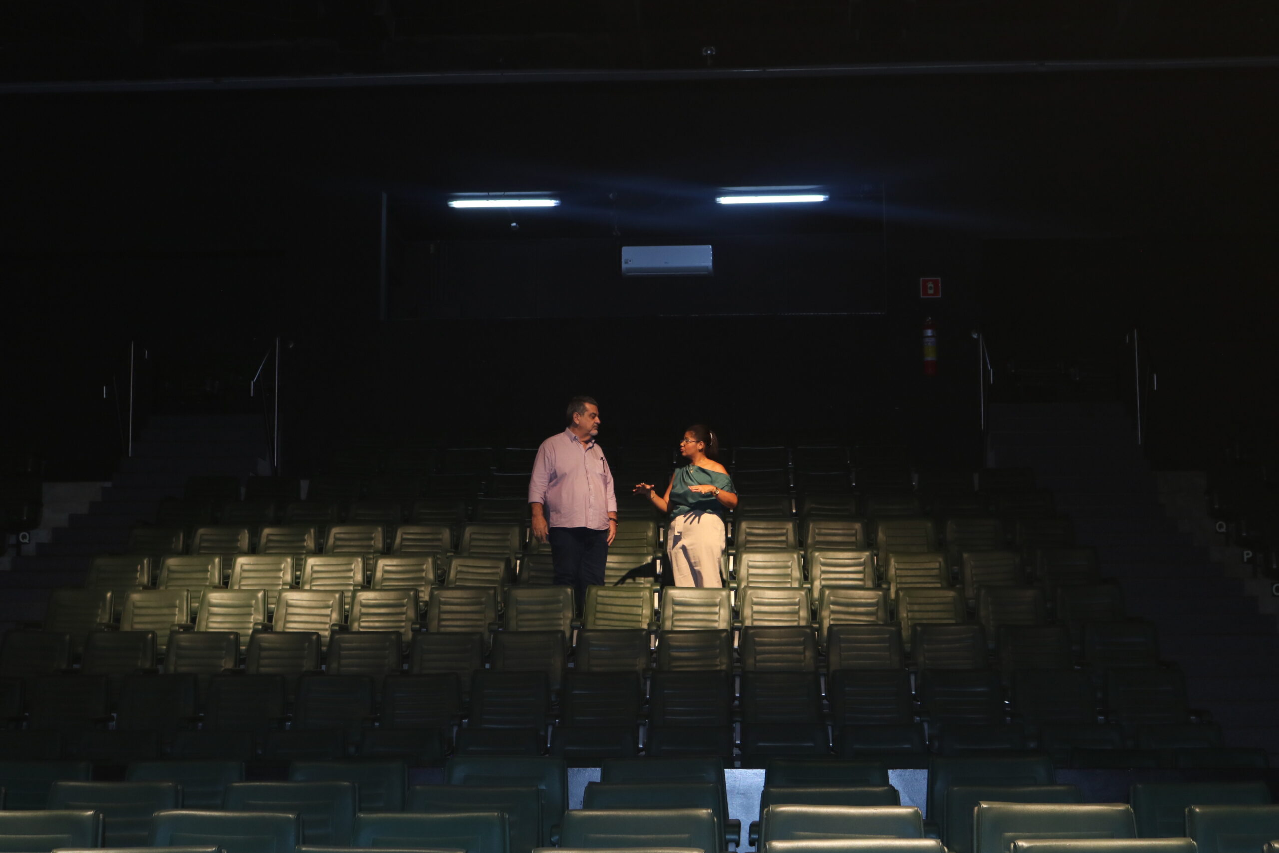 Um homem, o secretário Beltrame, e uma mulher, diretora Luana, em meio a poltronas do teatro