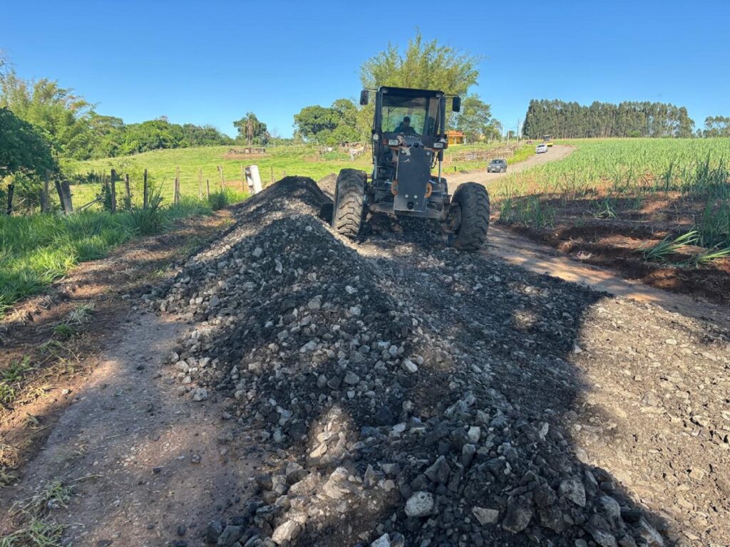 Trator passa com as rodas em cima de lajão britado em estrada rural.