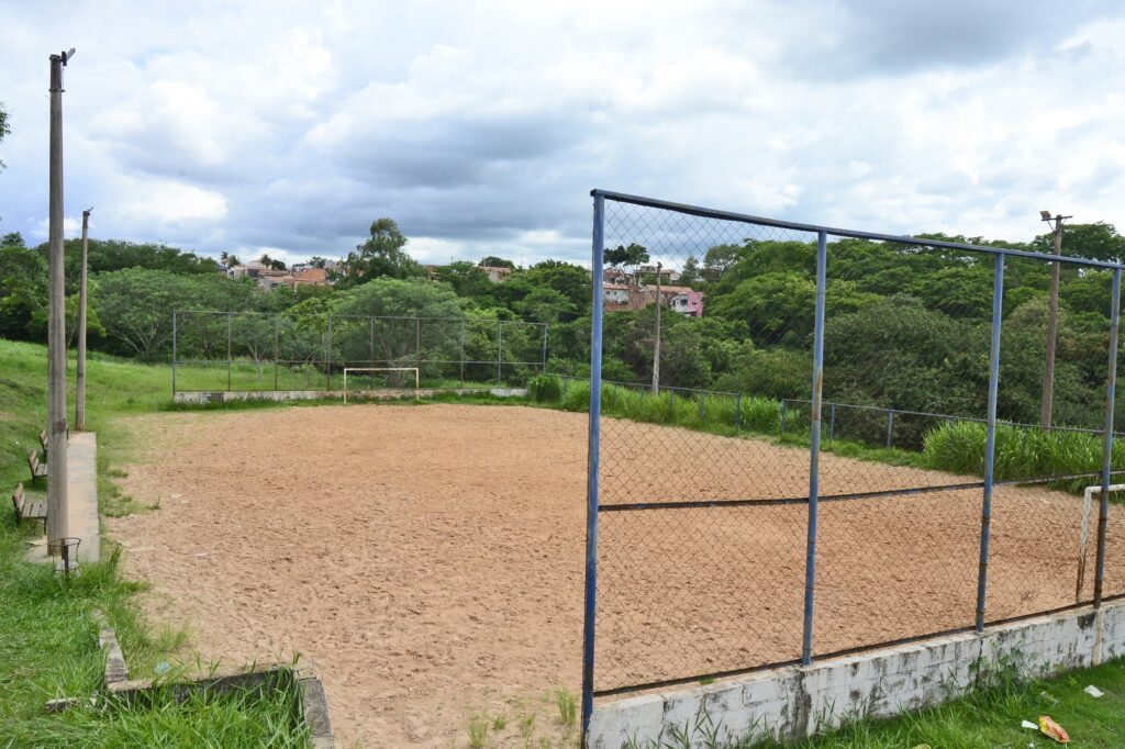 A foto mostra quadra de areia no Loteamento Santo Antônio onde será construída uma quadra poliesportiva.
Na imagem é possível ver uma quadra de areia, cercada por alambrados e muitas árvores e área verde.