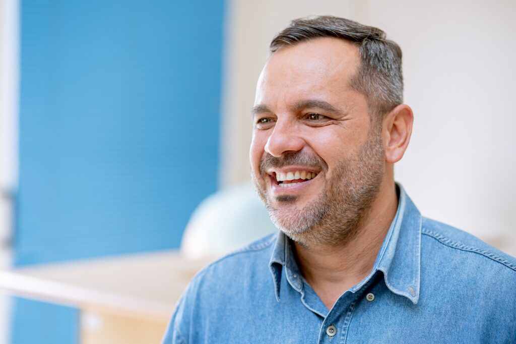 Jovem de camisa azul e sorridente concede entrevista.