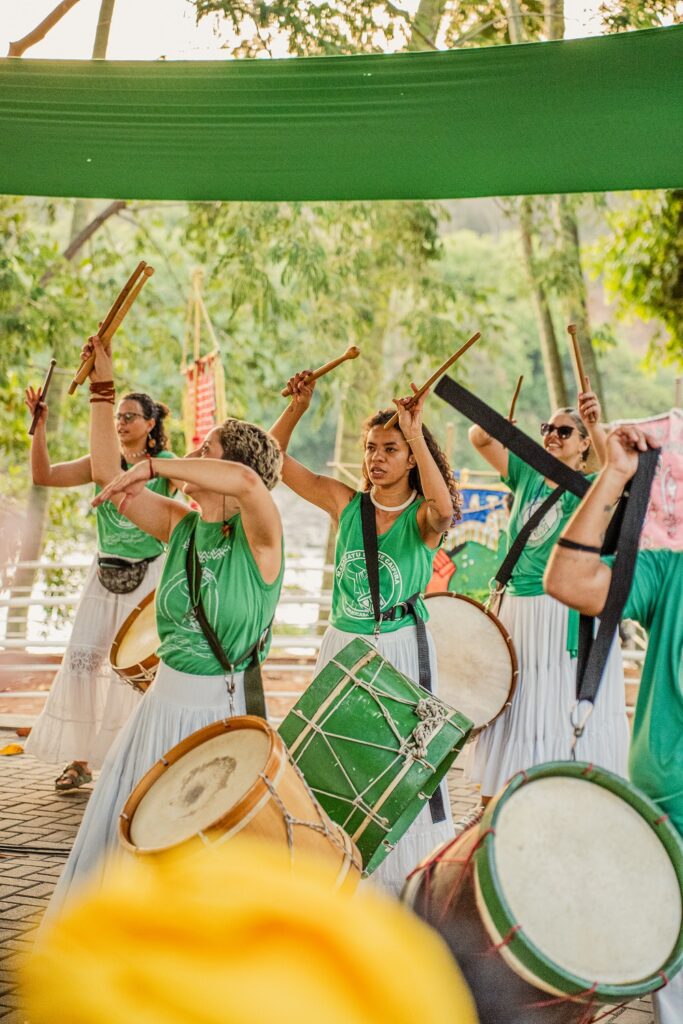 Homens e mulheres vestidos de branco e verde tocando tambores