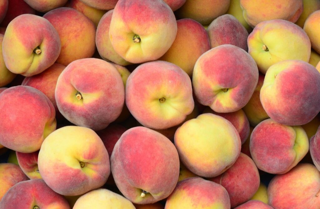 Vários pêssegos com parte na cor amarelo e vermelho, colocados um em cima do outro.