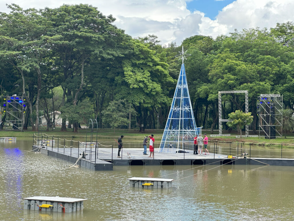Homens trabalham sob estrutura que flutua no lago do parque da rua do porto, em preparativo de espetáculo de Natal