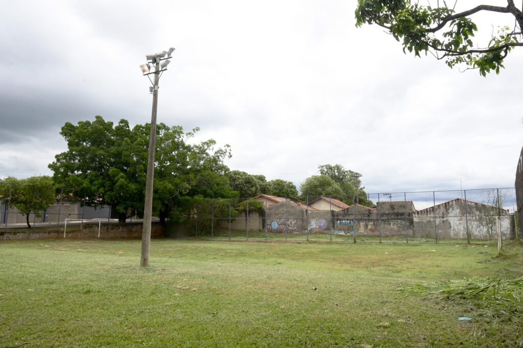 Na foto produzida no bairro Jupiá é possível ver uma quadra com areia, cercada por casas.
Existe uma árvore ao fundo da imagem e telhados das casas vizinhas.