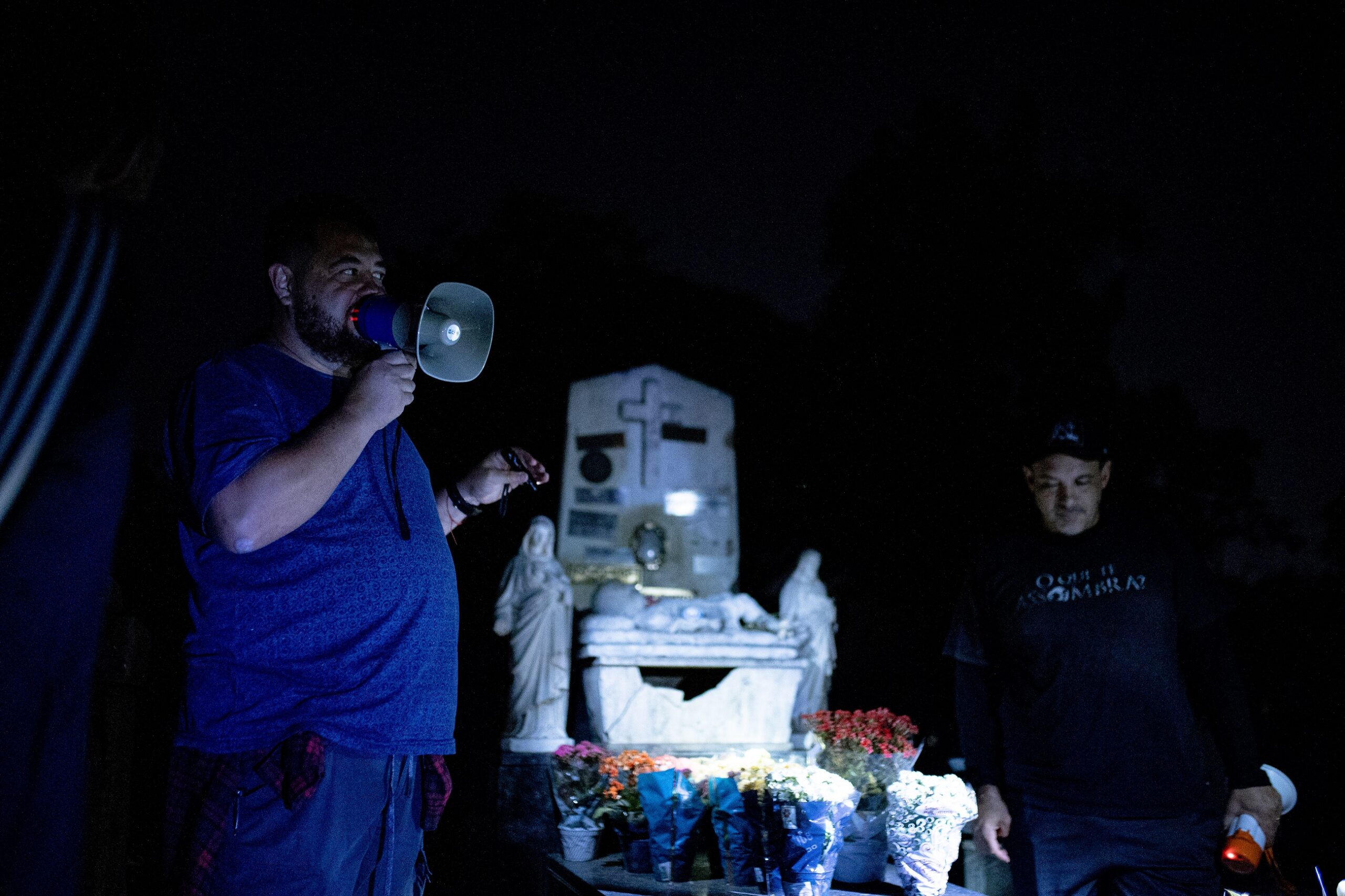 imagem mostra o cemitério da saudade durante a noite relembrando a última atividade. as pessoas estão com lanternas e o cemitério está completamente escura, criando um clima de medo nas pessoas