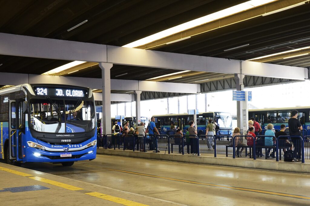 Ônibus azul do transporte público estaionado em uma das baias do Terminal Central de Integração. No outro lado aparece usuários e usuárias, que aguardam a chegada dos ônibus para seus bairros.