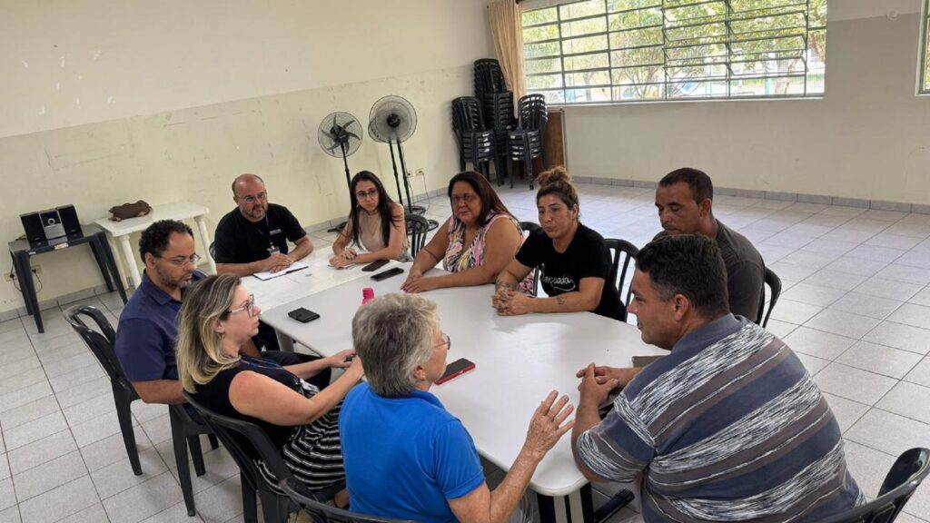 Grupo de 9 pessoas se reúnem em torno de uma mesa branca, para discutir possível ciação de cooperativa de recicladores.