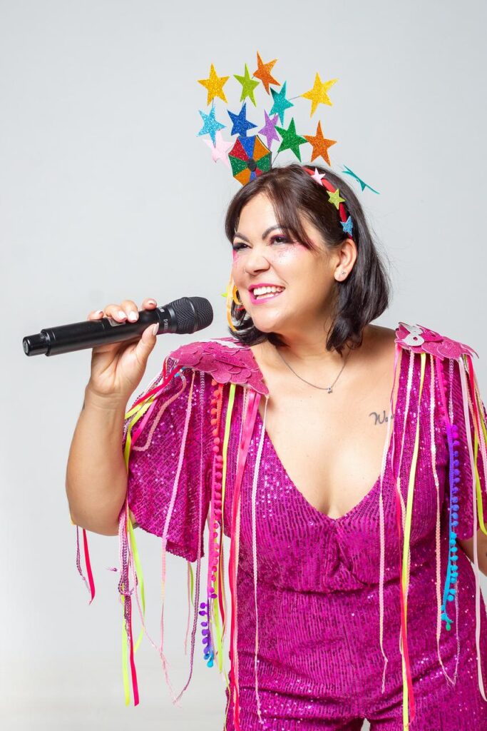 mulher com roupas rosa, alusiva ao Carnaval, com microfones nas mãos