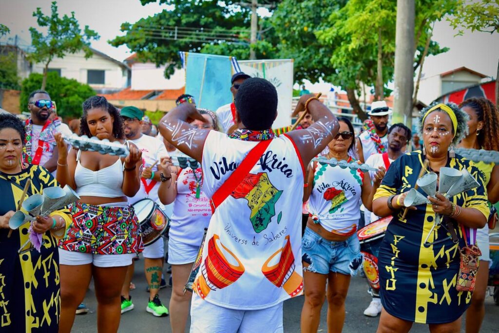 homens e mulheres dançando, com roupas coloridas e instrumentos musicais nas mãos