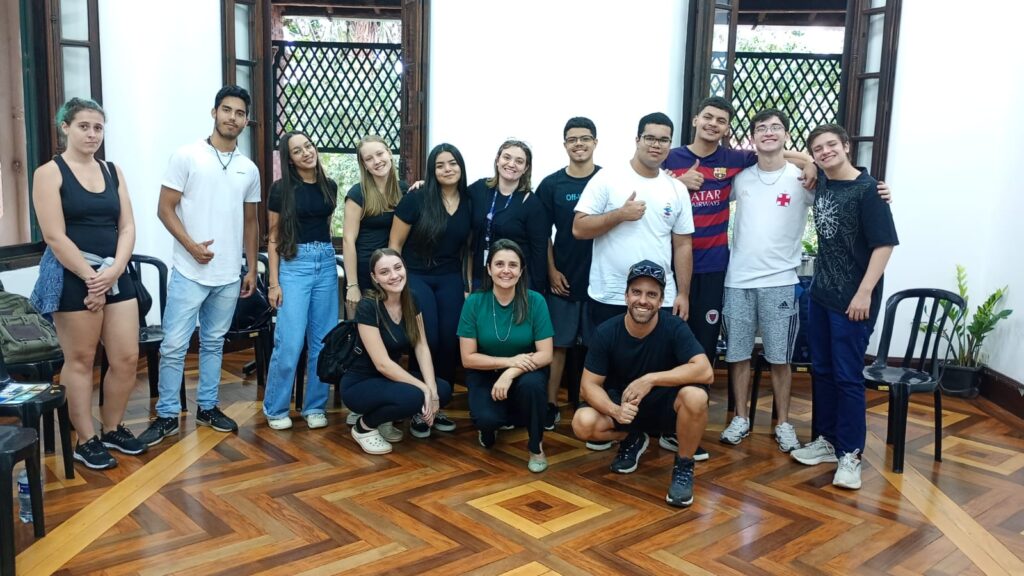 Uma imagem de grupo de jovens, possivelmente estudantes ou participantes de um evento, reunidos em uma sala.
