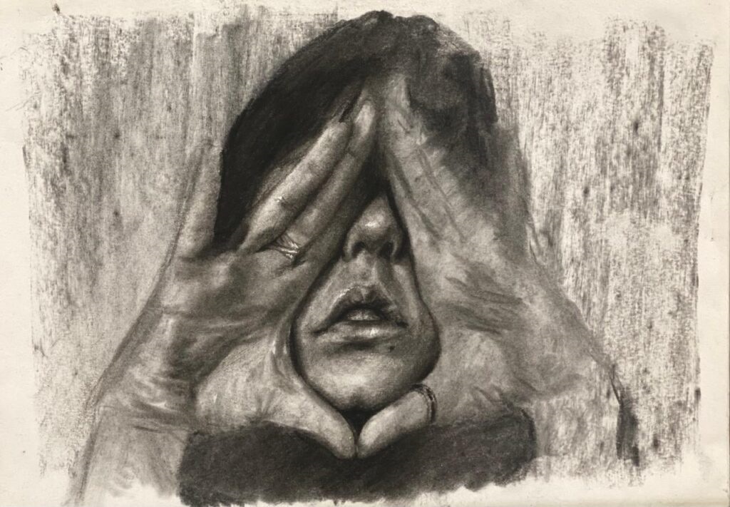 A imagem é um desenho a carvão de uma pessoa com as mãos cobrindo os olhos. O desenho é feito em tons de cinza escuro e claro, criando uma atmosfera sombria e introspectiva. O rosto da pessoa é parcialmente visível entre os dedos, mostrando uma expressão de sofrimento ou angústia. Os traços são expressivos e detalhados, principalmente nas mãos e no rosto, contrastando com o fundo mais texturizado e menos definido. A técnica utilizada sugere um trabalho de sombreamento cuidadoso, com variações de tom que dão profundidade e volume à figura. O estilo geral é realista, porém com uma certa carga emocional evidente.