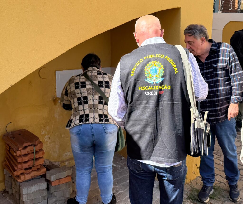 dois homens e uma mulher estão próximo a uma parede com uma pia e um ralo aparente, eles exercem ato de fiscalização ou algo similar