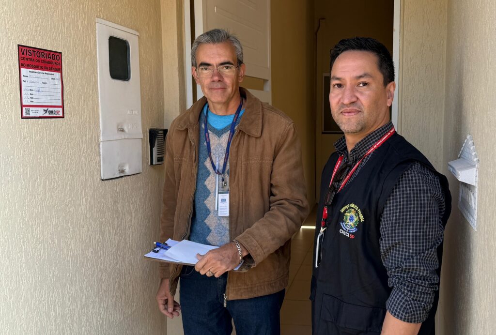 imagem mostra dois agentes fiscalizadores colocando um adesivo com os dizeres "fiscalizado" na parede