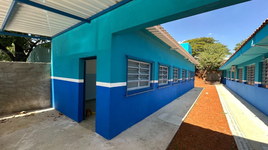 A imagem mostra a fachada de uma Unidade de Saúde da Família (USF) com a identificação "USF UNIDADE DE SAÚDE DA FAMÍLIA ARTEMIS I E II". A construção possui um telhado de metal aparente, sustentado por vigas azuis. As paredes são pintadas em duas tonalidades de azul, com uma faixa branca separando-as.