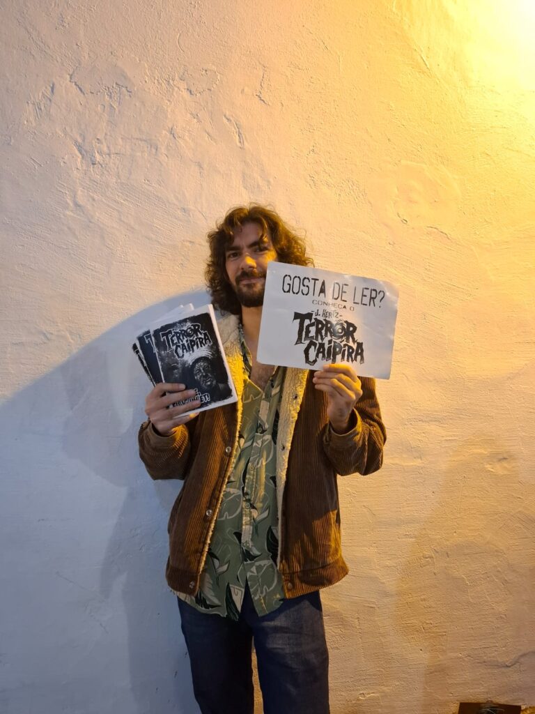 Músico e escritor Jedias Hertz segura livros e panfletos de sua obra “Terror Caipira”. Ele participa da programação com contação de histórias de suspense e música folk.