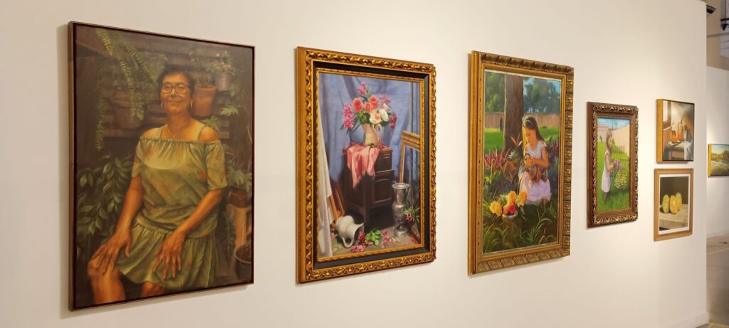  Parede exibe diversas pinturas emolduradas, incluindo retratos e naturezas-mortas.