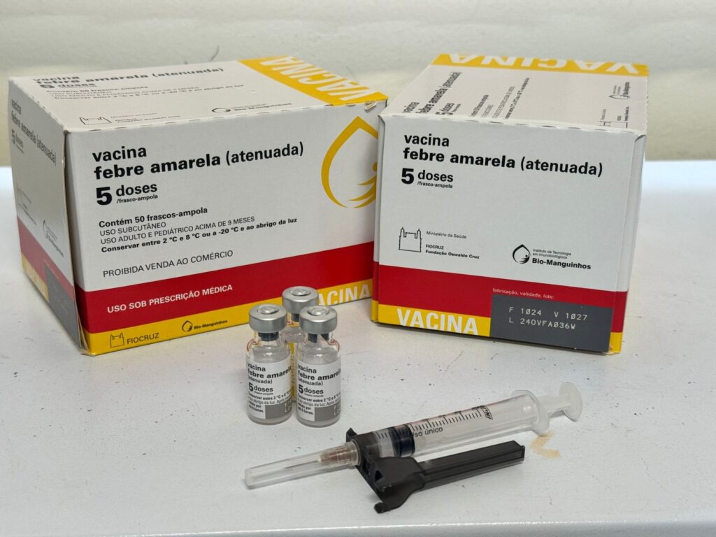A imagem mostra duas caixas de vacina contra a febre amarela (atenuada), juntamente com três frascos-ampola e uma seringa. *Detalhes nas caixas:* * *Nome do produto:* Vacina febre amarela (atenuada) * *Quantidade:* 5 doses / frasco-ampola * *Conteúdo:* Contém 50 frascos-ampola * *Via de administração:* USO SUBCUTÂNEO * *Indicação:* USO ADULTO E PEDIÁTRICO ACIMA DE 9 MESES * *Armazenamento:* Conservar entre 2 °C e 8 °C ou a -20 °C e ao abrigo da luz. * *Restrição de venda:* PROIBIDA VENDA AO COMÉRCIO * *Prescrição:* USO SOB PRESCRIÇÃO MÉDICA * *Fabricante:* FIOCRUZ - Fundação Oswaldo Cruz, Instituto de Tecnologia em Imunobiológicos - Bio-Manguinhos. * *Informações de fabricação/lote:* F 1024 V 1027 L 240VFA036W *Frascos-ampola e seringa:* * Três frascos-ampola de vidro, com rótulos que indicam "Vacina febre amarela (atenuada)" e "5 doses". * Uma seringa descartável com uma agulha acoplada.