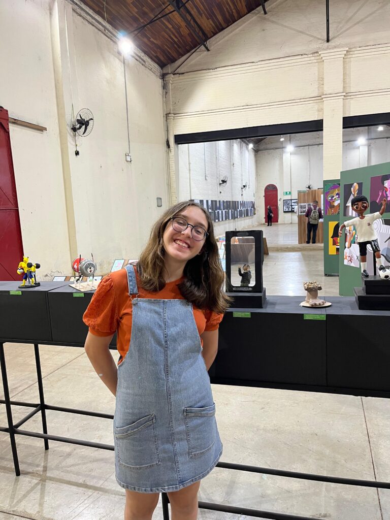 Jovem sorri em frente a esculturas expostas em pedestais no Salãozinho de Humor.