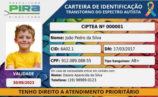 A imagem é de uma carteira de identificação para pessoas com Transtorno do Espectro Autista (TEA), emitida pela Prefeitura de Piracicaba. A carteira apresenta a foto de um menino sorridente, com os braços cruzados e vestindo uma camiseta amarela. Os dados contidos na carteira incluem: * *CIPTEA Nº:* 000001 * *Nome:* João Pedro da Silva * *CID:* 6A02.1 * *DN (Data de Nascimento):* 17/03/2017 * *CPF:* 912.089.088-55 * *Tipo Sanguíneo:* AB+ * *Validade:* 30/09/2023 Há também um campo para contato em caso de necessidade, com o nome de Daiane Aparecida da Silva e o telefone (19) 98989-0123. Na parte inferior da carteira, destaca-se a frase "TENHO DIREITO A ATENDIMENTO PRIORITÁRIO", reforçando os direitos garantidos pela identificação. O design da carteira é colorido, com um fundo que remete a peças de quebra-cabeça, símbolo frequentemente associado ao autismo.