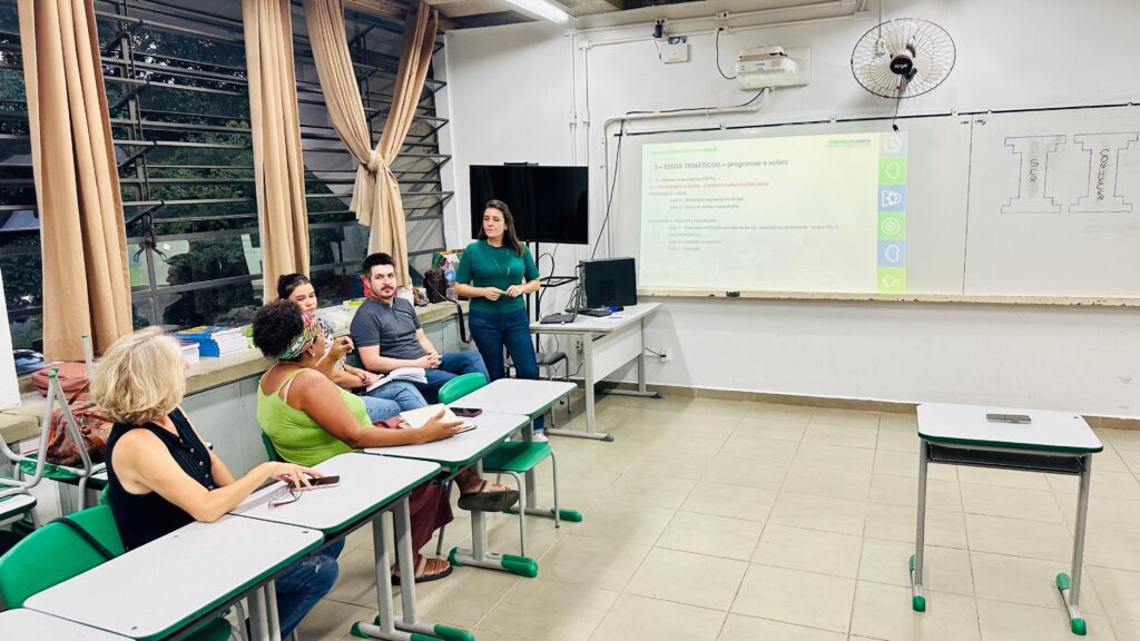 Imagem mostram pessoas, entre homens e mulheres, durante a realização de uma reunião em uma sala de aula