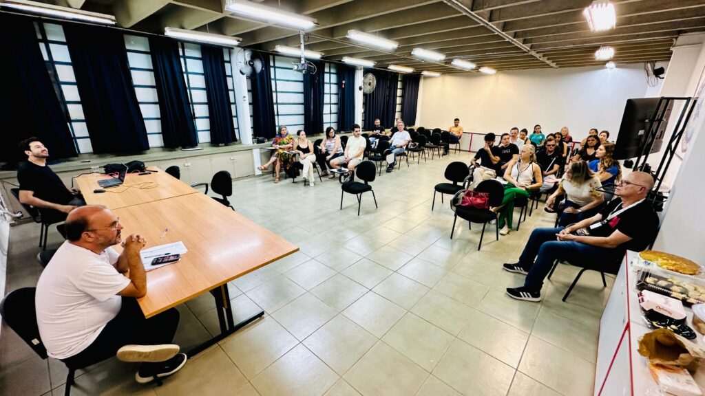 Imagem mostram pessoas, entre homens e mulheres, durante a realização de uma reunião em uma sala de aula