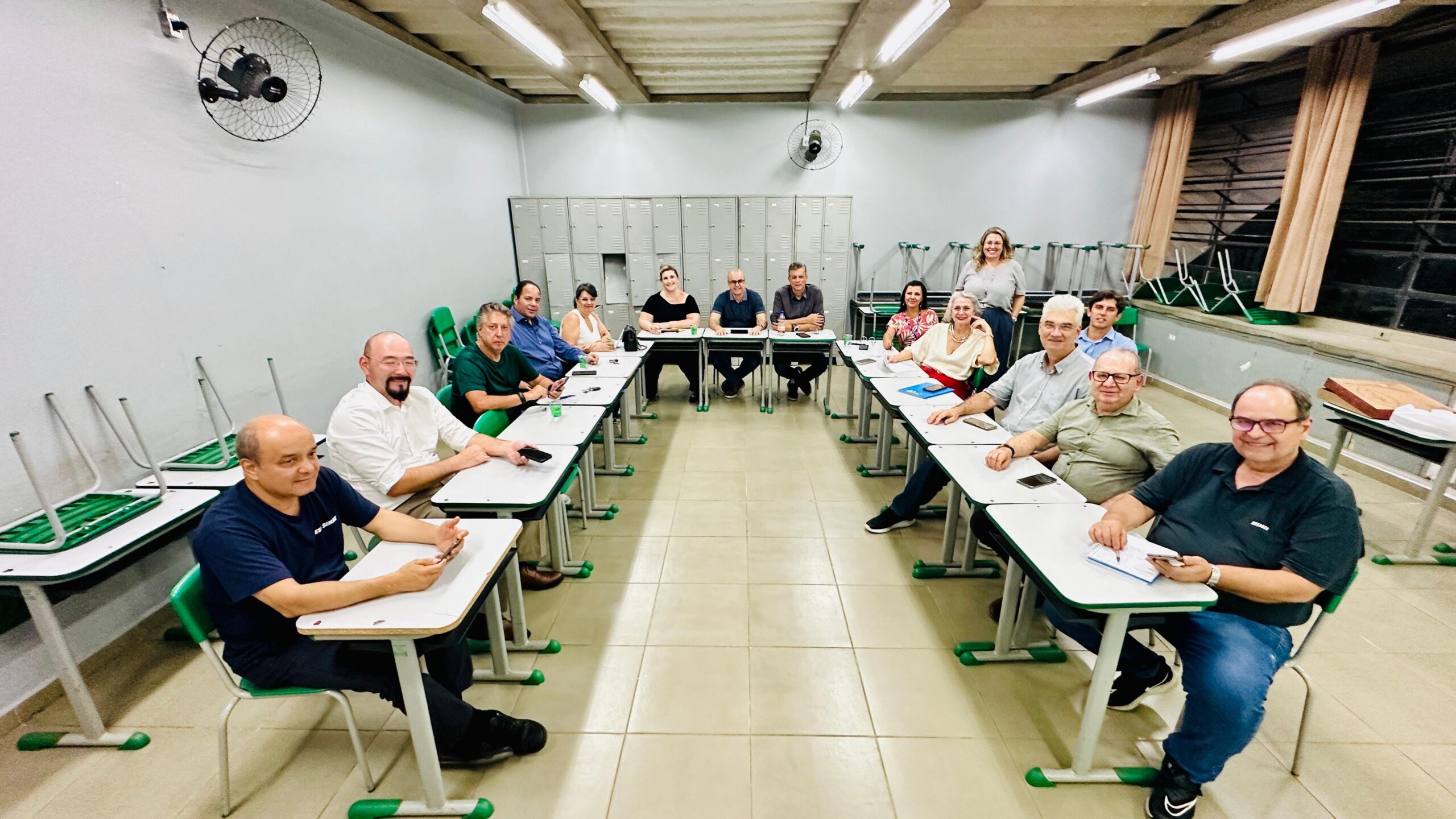 Imagem mostram pessoas, entre homens e mulheres, durante a realização de uma reunião em uma sala de aula