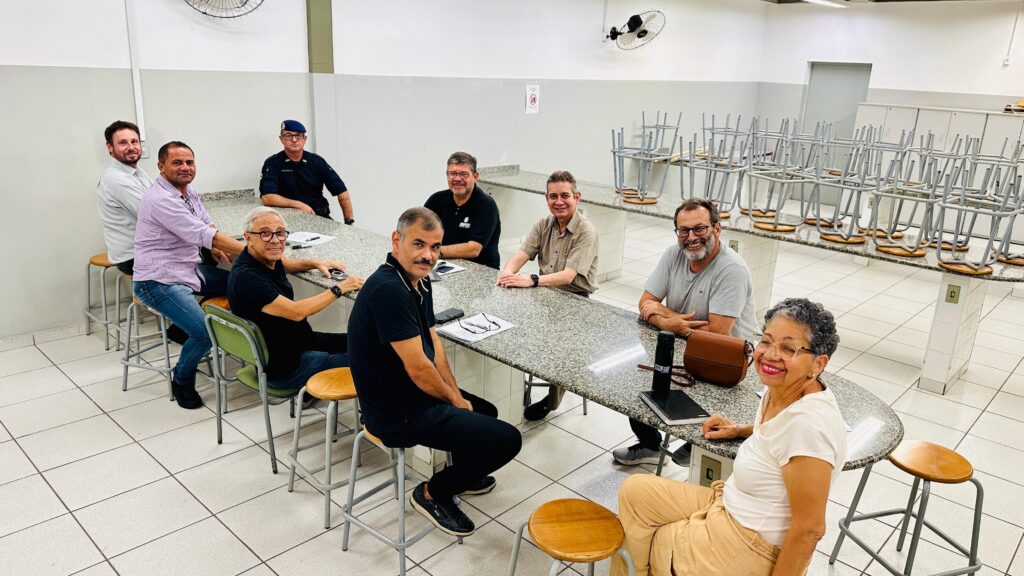 Imagem mostram pessoas, entre homens e mulheres, durante a realização de uma reunião em uma sala de aula