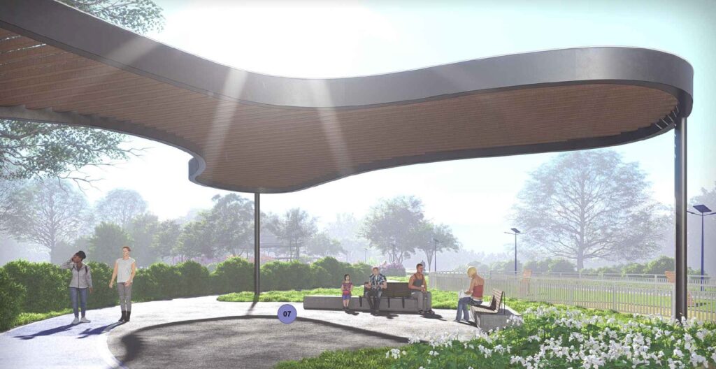 A imagem mostra uma renderização arquitetônica de um pavilhão moderno em um parque. O pavilhão tem uma cobertura com formato orgânico e ondulado, com uma estrutura metálica escura e um forro de ripas de madeira. A cena é iluminada por uma luz suave, provavelmente do início da manhã ou fim da tarde, com raios de sol visíveis que passam através da cobertura. No entorno do pavilhão, há bancos modernos feitos de pedra e madeira, onde algumas pessoas estão sentadas e outras caminhando ou brincando. O parque é bem cuidado, com gramado verde, canteiros de flores brancas e árvores densas ao fundo. O céu está claro e levemente enevoado. No chão, próximo ao pavilhão, há um círculo roxo com o número "07", possivelmente uma marcação para identificação do local ou projeto. A composição transmite uma sensação de espaço público contemporâneo, convidativo e integrado à natureza.