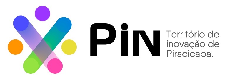 A imagem mostra o logotipo do "PiN - Território de inovação de Piracicaba". À esquerda, há um símbolo abstrato e colorido formado por duas barras arredondadas que se cruzam, criando um formato parecido com um "X". Em torno dessas barras, há seis círculos coloridos, em tons de roxo, azul, verde, rosa, laranja e amarelo, com efeitos de transparência onde as formas se sobrepõem. À direita do símbolo, está escrito "PiN" em uma fonte preta, moderna e em negrito, com o "i" em minúsculo e um ponto destacado. Abaixo e à direita do "PiN", há o texto "Território de inovação de Piracicaba." em uma fonte cinza, menor e também moderna, distribuído em três linhas. O fundo da imagem é branco, destacando as cores vivas do símbolo e o texto em preto e cinza. O logotipo transmite uma ideia de inovação, modernidade e diversidade, relacionada a um espaço ou iniciativa voltada para inovação na cidade de Piracicaba.