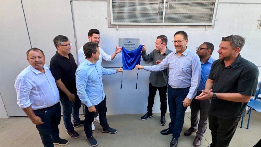 Na imagem aparece oito homens sorridentes ao lado de um aplaca de inauguração. Ao fundo aparece um homem de camisa branca sorridente e ao lado um senhor de óculos que seguram um tecido azul que foi tirado da placa.