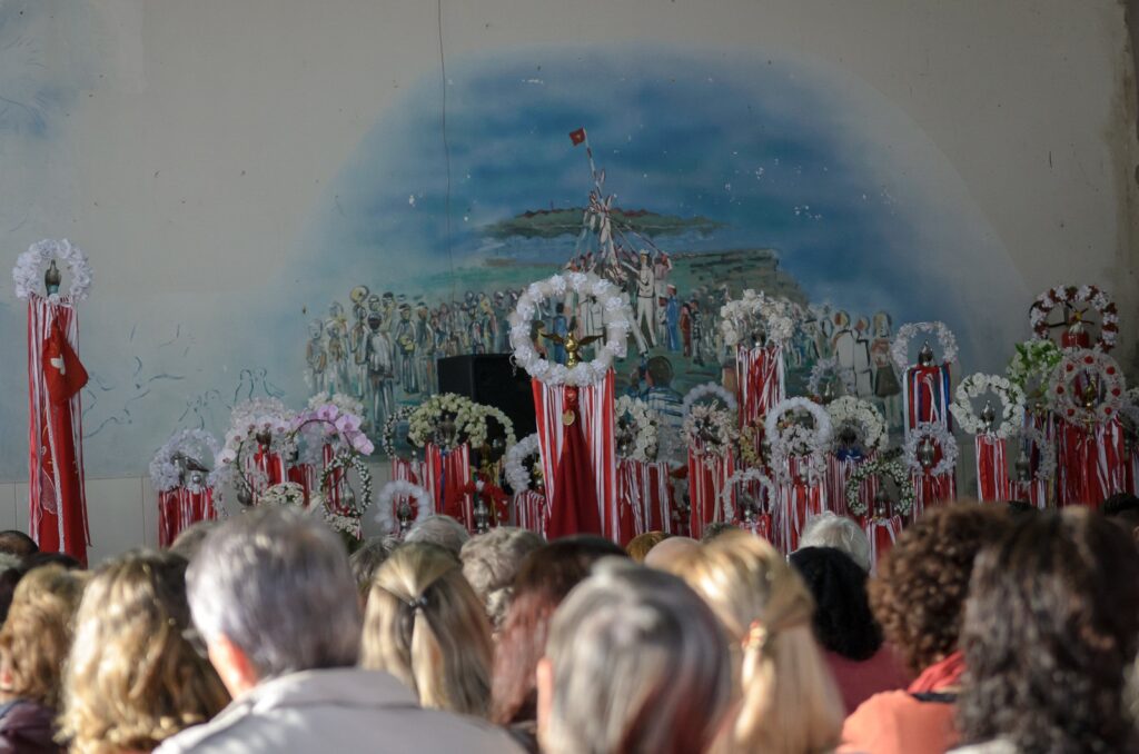 Essa é uma imagem muito bonita e cheia de significado! Ela captura perfeitamente o espírito de uma celebração tradicional, com as coroas decoradas e as fitas coloridas criando um ambiente muito acolhedor e festivo. O mural ao fundo traz um contexto histórico e cultural fascinante para a cena, mostrando como essas tradições são vivas e valorizadas pela comunidade. Dá para sentir o respeito e a dedicação das pessoas que estão ali reunidas para manter viva essa cultura, né? É um momento muito especial de união e partilha