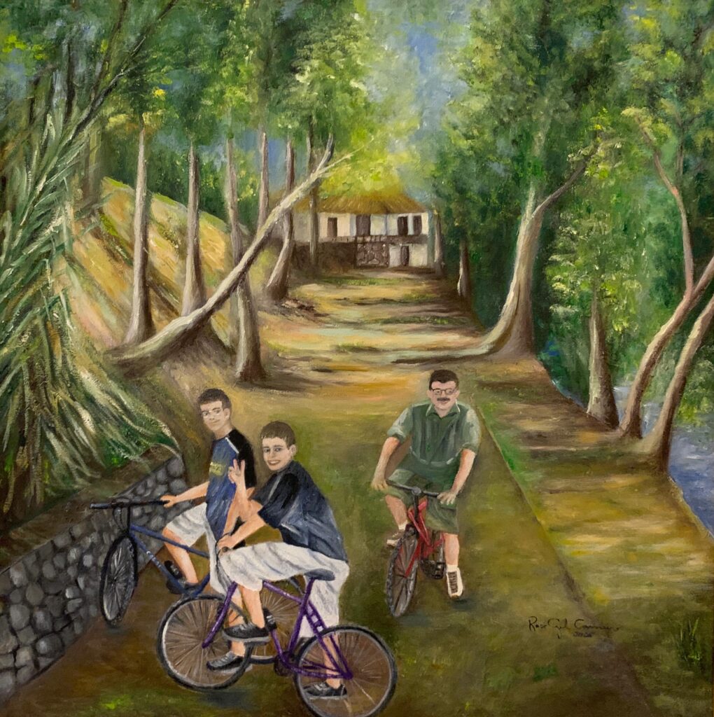 A imagem mostra uma pintura a óleo que retrata três pessoas andando de bicicleta por uma trilha de terra em meio a uma paisagem natural exuberante. Na cena, dois jovens aparecem na frente, um vestindo camiseta azul e shorts brancos, e o outro com camiseta escura e calça clara, fazendo sinal de paz com a mão. Ao lado deles, um homem mais velho, de óculos e bigode, veste uma camiseta verde e shorts e pedala uma bicicleta vermelha. Ao fundo, há uma pequena casa rústica cercada por árvores altas e densas, que formam um ambiente de floresta ou parque. A luz do sol ilumina suavemente o cenário, criando sombras e realces que dão vida à pintura. À esquerda, há um muro de pedras que acompanha o caminho, e à direita é possível ver um pequeno curso d’água. A assinatura do artista, "Rose Gil Camys 2006", está no canto inferior direito. O estilo da pintura é impressionista, com pinceladas visíveis que conferem textura e movimento à imagem.