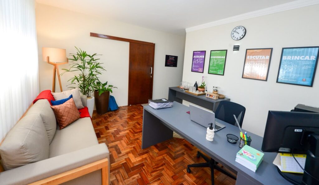 A foto mostra uma sala de atendimento equipada com mesa de trabalho, sofá para acolhimento, decoração aconchegante e cartazes educativos voltados à prevenção e ao fortalecimento dos vínculos familiares.