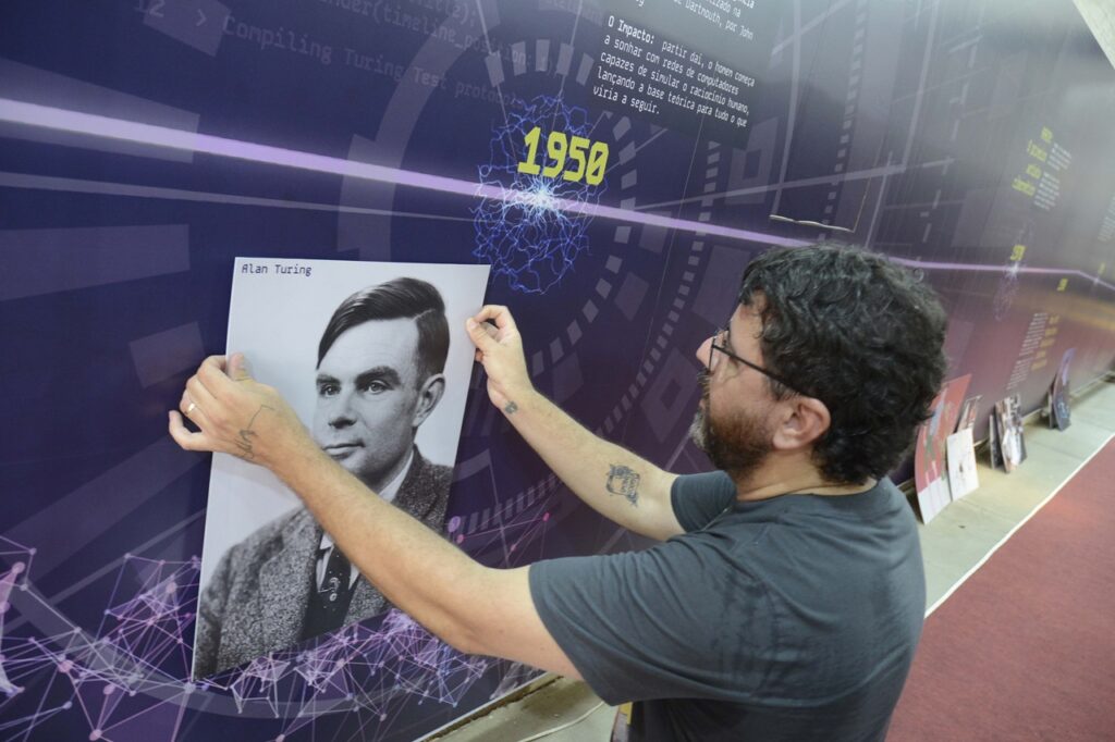 A imagem mostra uma exposição sobre arte computacional, destacando o período dos anos 1960 como o nascimento dessa forma de expressão artística. No painel, há textos explicativos em português e uma linha do tempo que segue pelas décadas seguintes.